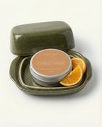 Body butter in a green container with oranges on a white background