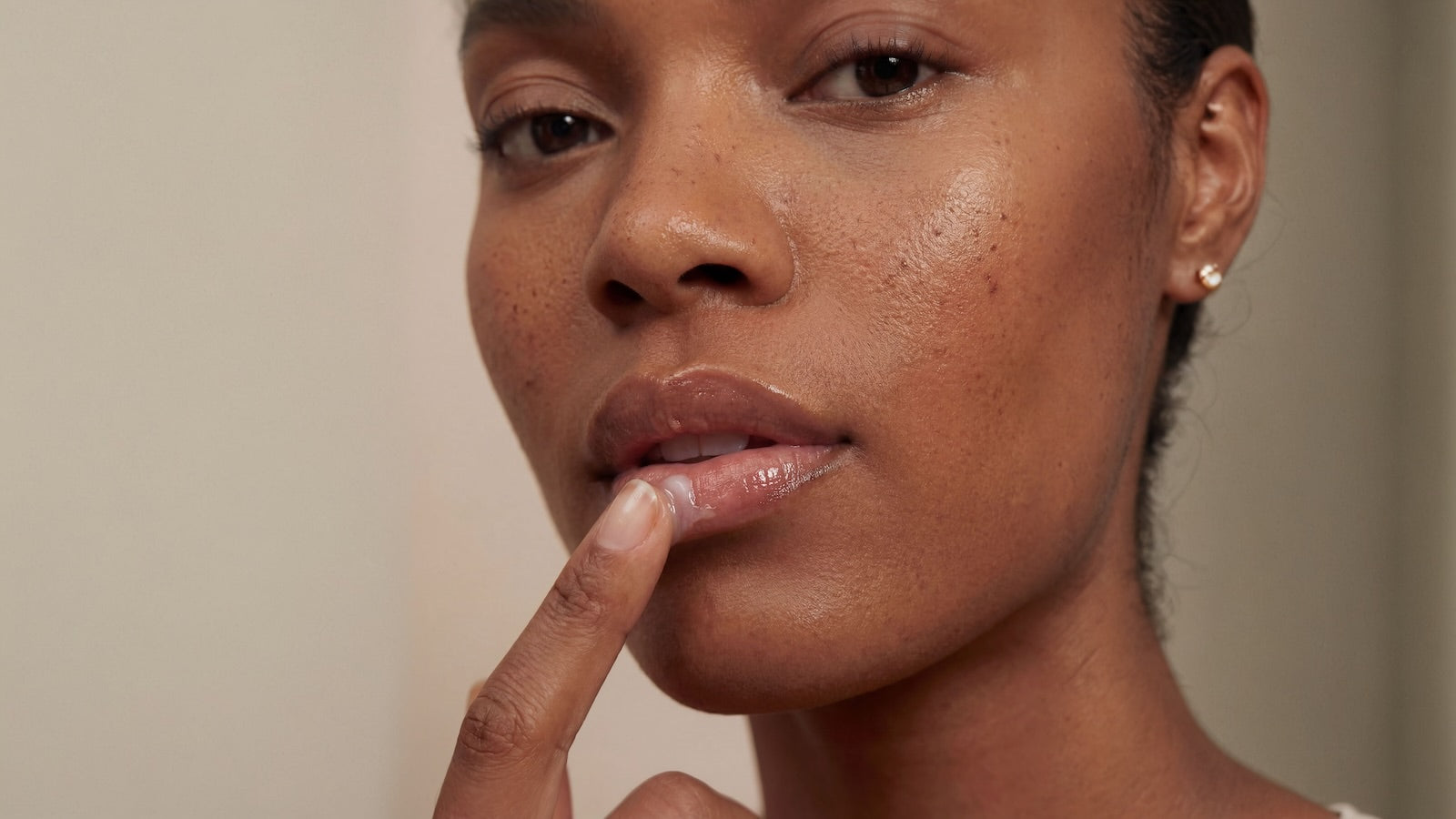 Woman applying lip butter with a neutral background