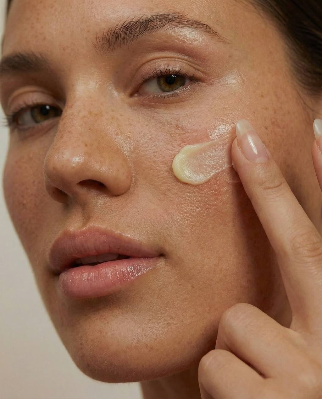Woman applying cream to her face with a neutral background