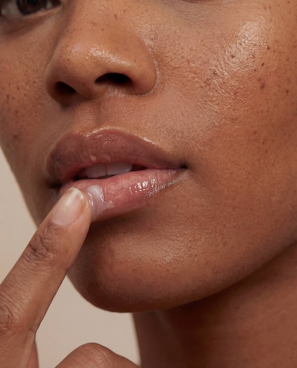 Close-up of a person applying lip butter against a neutral background
