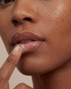 Close-up of a person applying lip butter against a neutral background