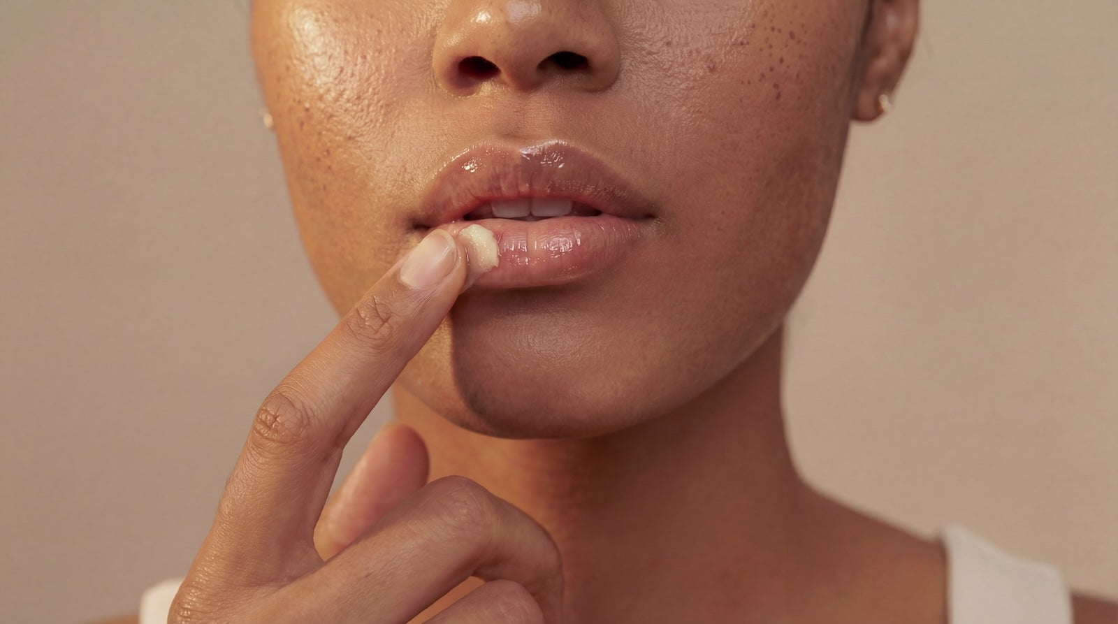 Close-up of a person applying lip butter against a beige background