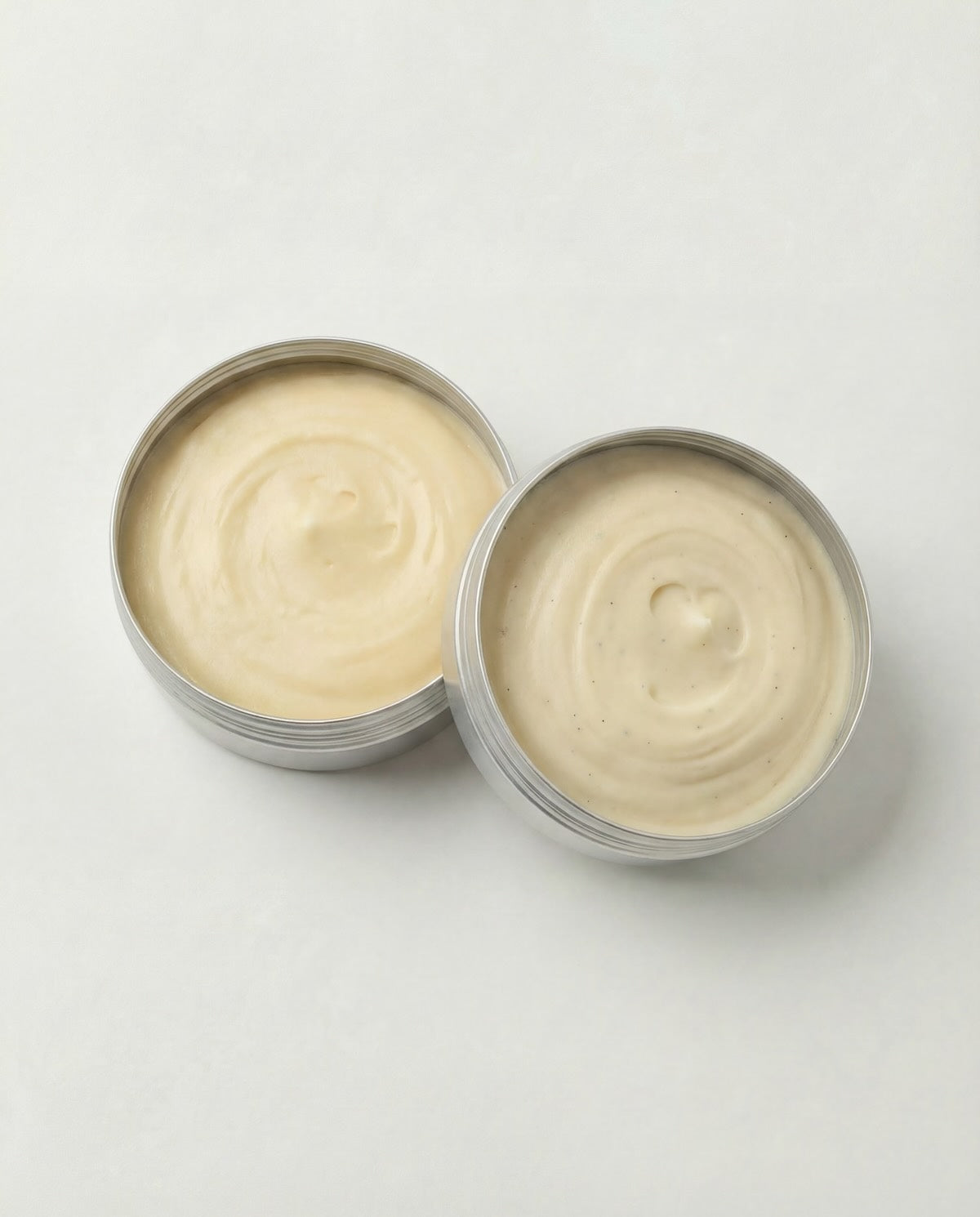 Two open tins of cream on a light gray background