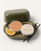 Two tins of Veld Skin body butter on a green tray with an orange slice and vanilla beans. 