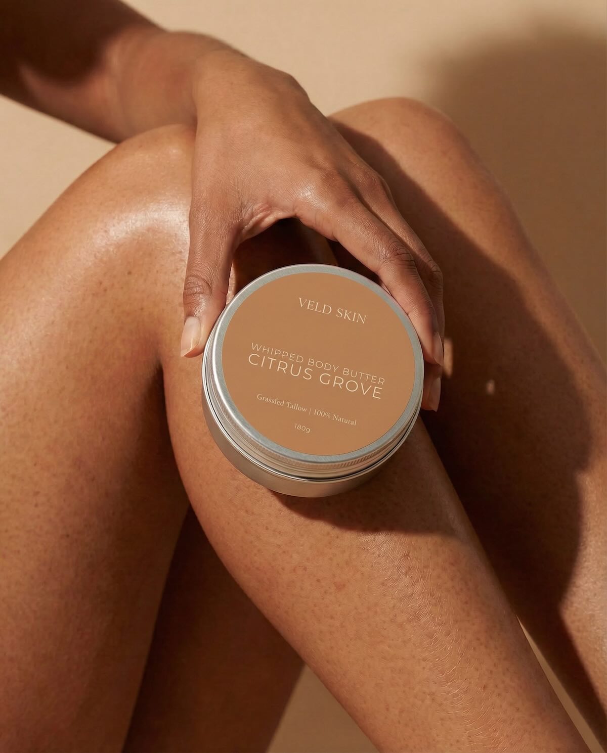Person holding a container of Veld Skin whipped body butter with 'Citrus Grove' scent on a beige background
