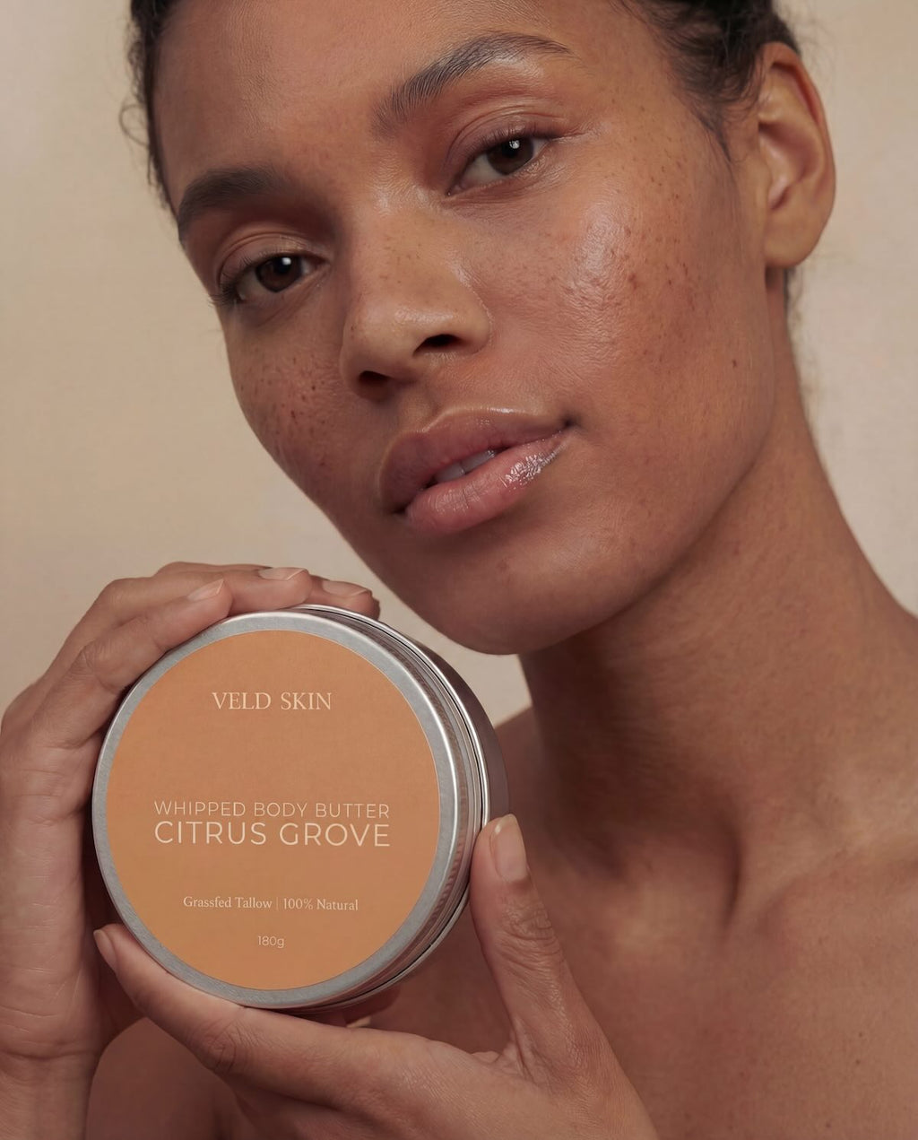 Woman holding a Veld Skin whipped body butter container labeled 'Citrus Grove' against a neutral background.