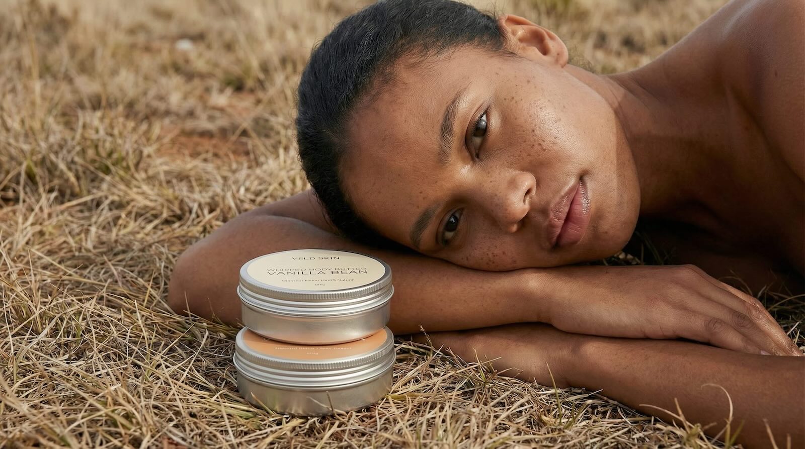 Person lying on dry grass with a skincare product container in front