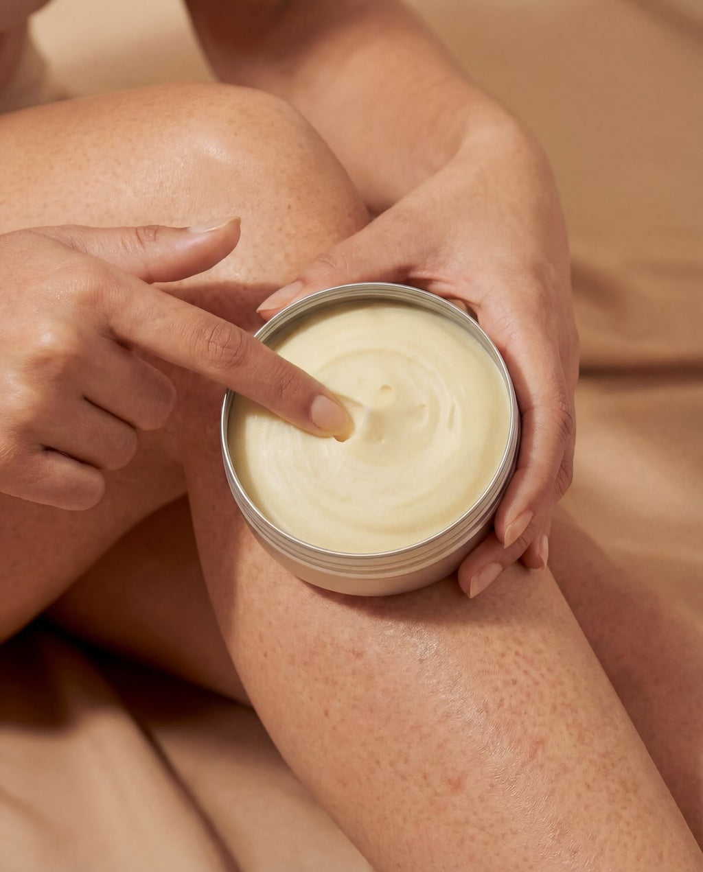 Person applying cream from a jar to their leg with a neutral background