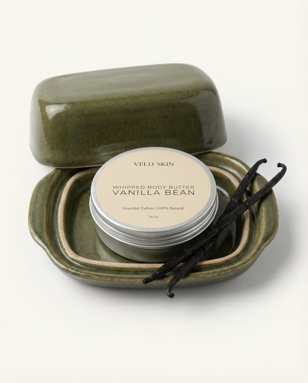 Whipped body butter in a green container with vanilla beans on a white background