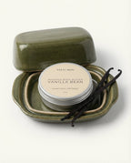 Whipped body butter in a green container with vanilla beans on a white background